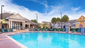 A swimming pool with lounge chairs and a covered seating area, surrounded by buildings with a classic architectural style. - Charming 3brtownhome Near Disney (Kissimmee)