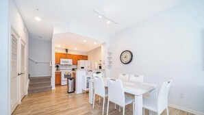A modern kitchen with white appliances, a dining area with white chairs, and a staircase leading to another level. - Charming 3brtownhome Near Disney (Kissimmee)