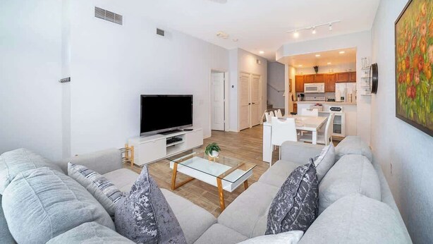A modern living room with a flat-screen TV, grey sofa, and a glass coffee table. - Charming 3brtownhome Near Disney (Kissimmee)