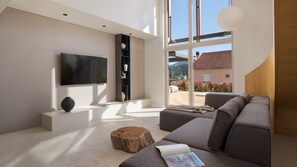 A modern living room with a large TV, a bookshelf, a sofa, and a view of the outdoors.