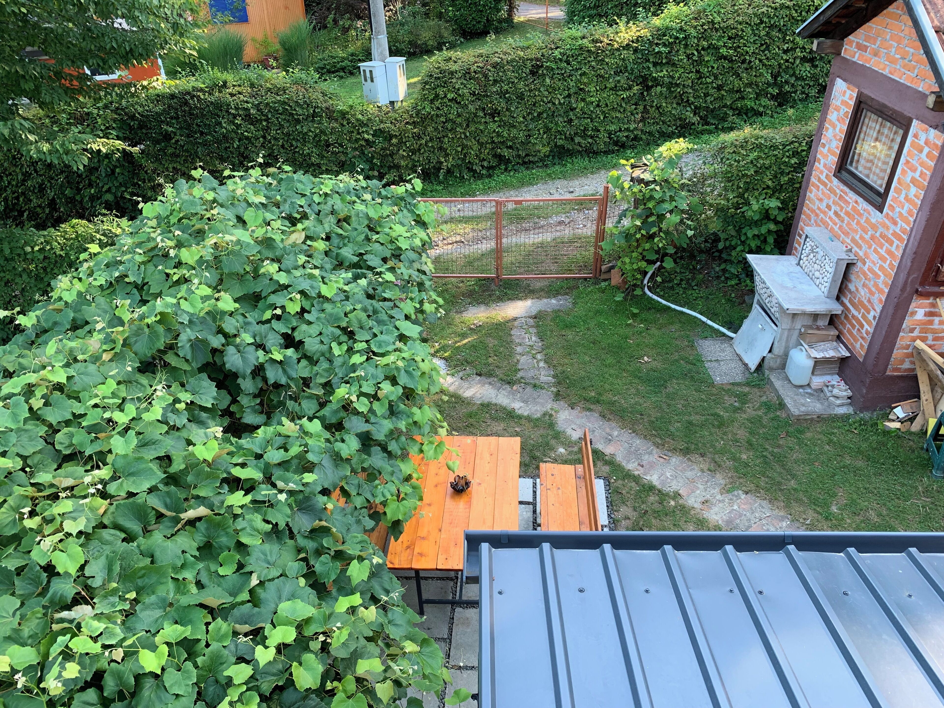 A garden area with a wooden table, a metal roof, and a brick building.
