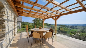 A wooden pergola with a round table and chairs, overlooking a scenic landscape.