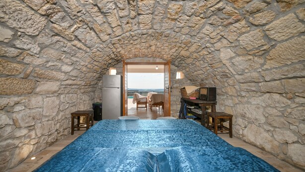 A stone-walled room with a bed, a table, and a television.