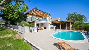 A two-story house with a pool, outdoor seating, and a wooden pergola.