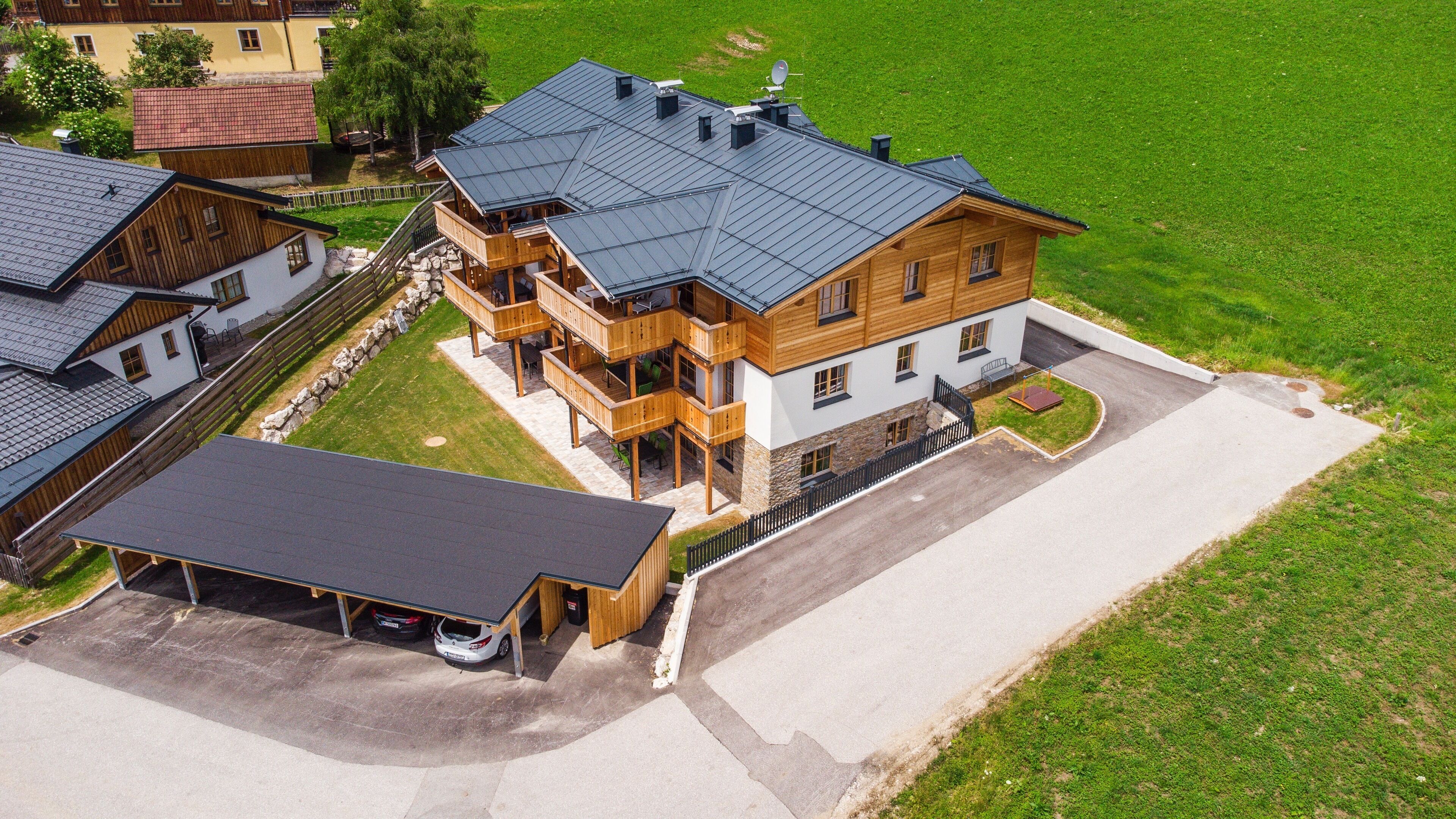 A multi-story wooden house with a balcony, a covered carport, and a driveway.