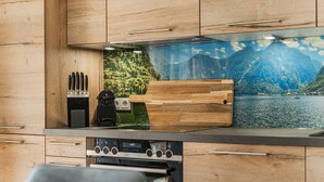 A modern kitchen with wooden cabinets, a built-in stove, and a scenic mural of a lake and mountains. - Dachstein West Apartment 1a (Russbach am Pass Gschuett)
