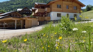 A wooden chalet with multiple balconies and a white facade, surrounded by lush greenery and a mountainous backdrop. - Dachstein West Apartment 1a (Russbach am Pass Gschuett)