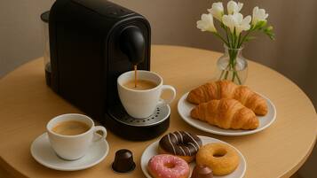 Eine Kaffeemaschine, zwei Kaffeetassen, Croissants, Donuts und eine Vase mit Blumen auf einem runden Tisch.