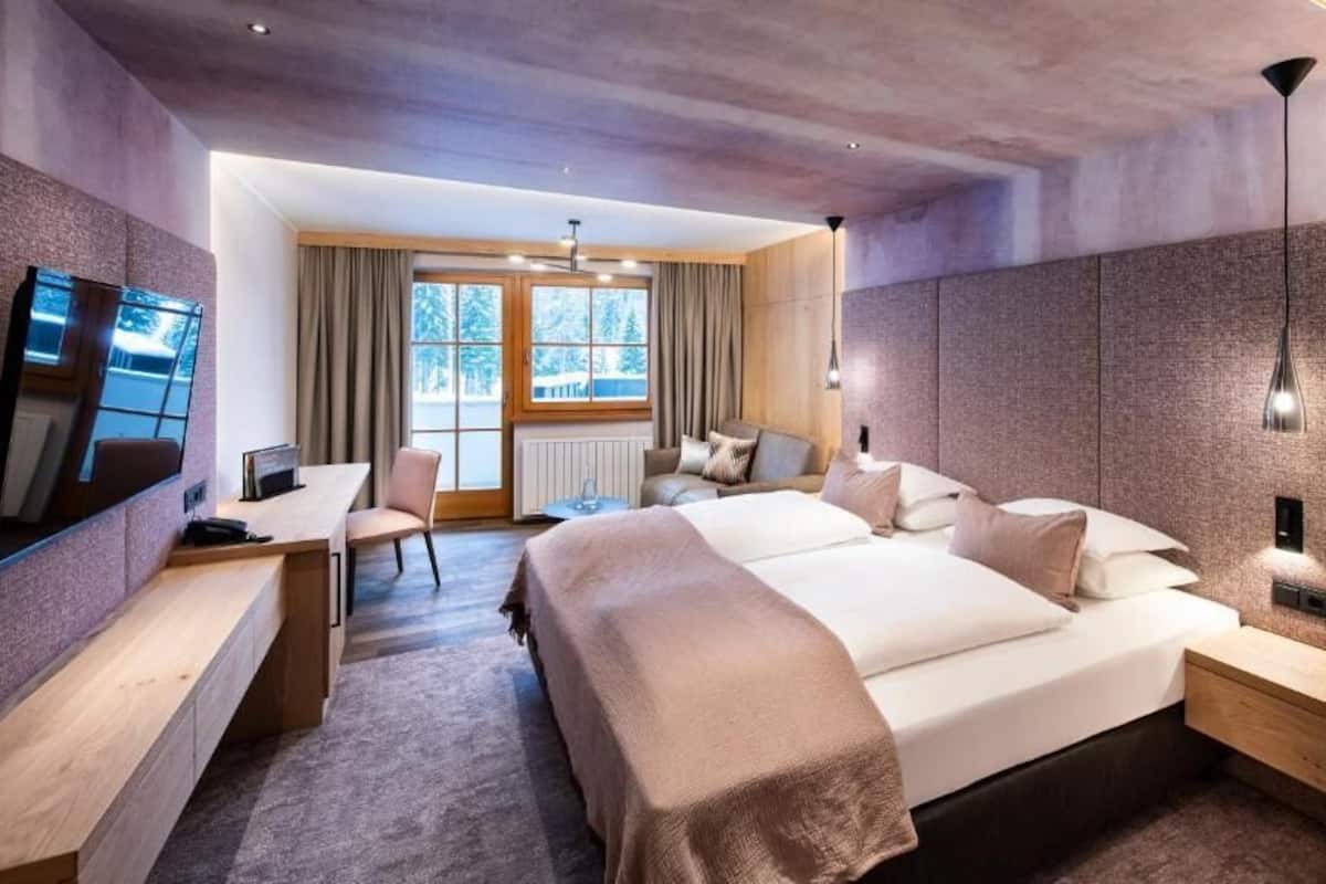 A modern hotel room with a large bed, a desk, a chair, and a TV.
