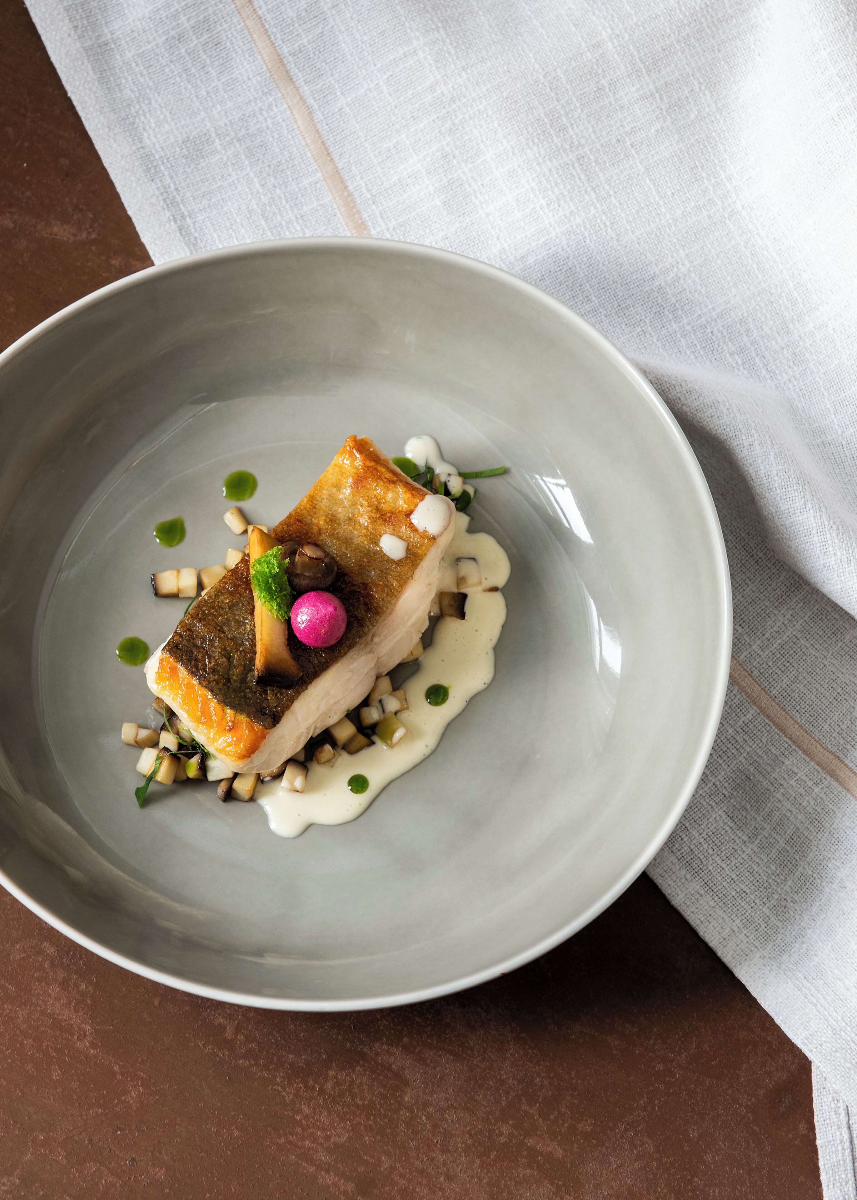 A plate with a piece of fish, some vegetables, and a sauce.