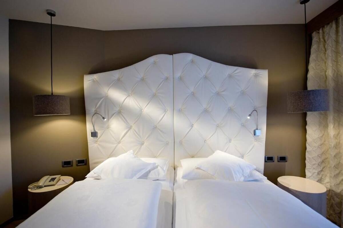A double bed with a tufted headboard, bedside lamps, a phone on a nightstand, and a round table with a lamp.