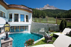 A pool area with a stone wall, lounge chairs, and a mountain view. - Hotel Sonnalp (Nova Ponente)