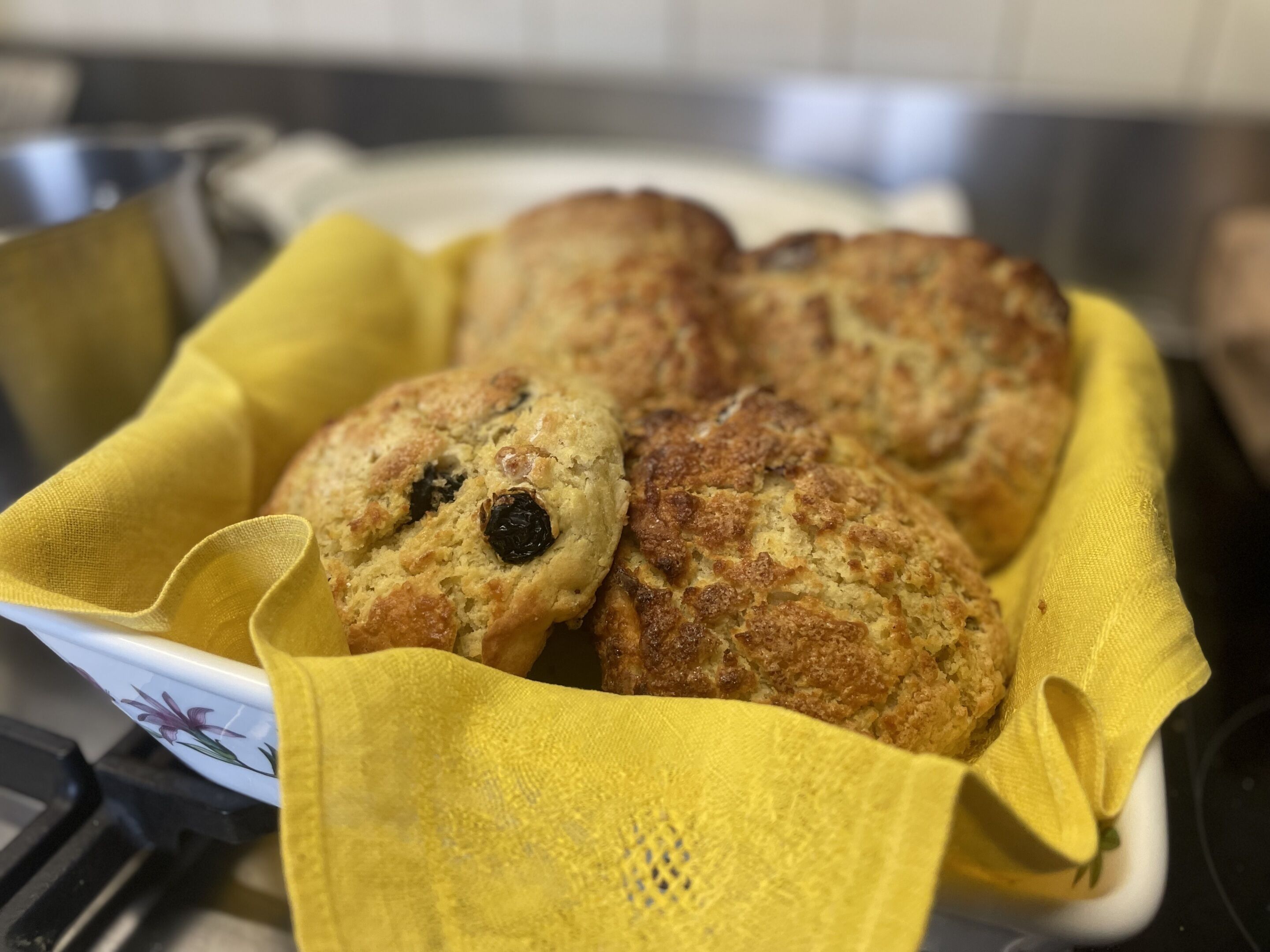 Een dienblad met versgebakken scones met rozijnen, op een gele doek geplaatst.