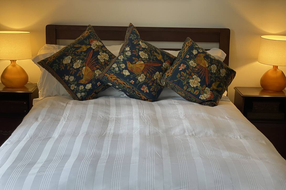 Un letto con biancheria a righe e tre cuscini decorativi con motivi floreali e di uccelli.
