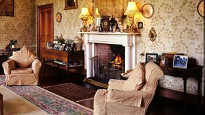 Un salón tradicional con chimenea, dos sillones, un alfombra estampada y adornos sobre la repisa.