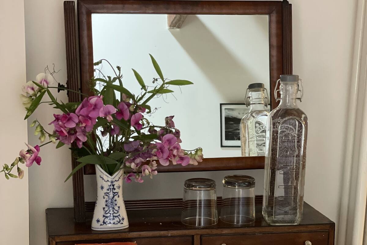 Una scrivania in legno con un vaso di fiori, uno specchio e una pila di libri.