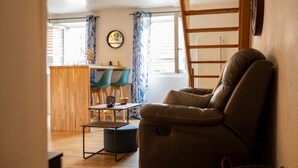 A living room with a leather sofa, a wooden dining table with chairs, and a kitchen area in the background.