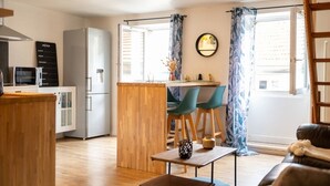 A compact kitchen with a refrigerator, microwave, and wooden counter. There is a dining area with a table and chairs, and a small seating area with a couch.