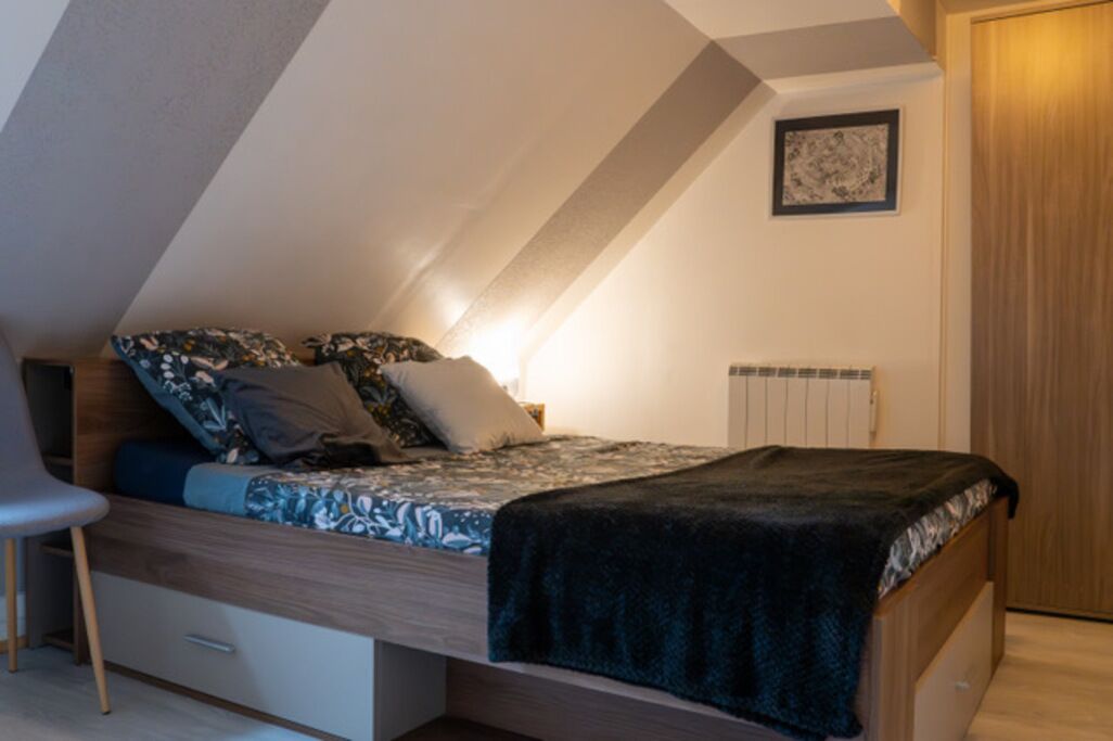 A bedroom with a bed, a chair, a radiator, and a wooden door.