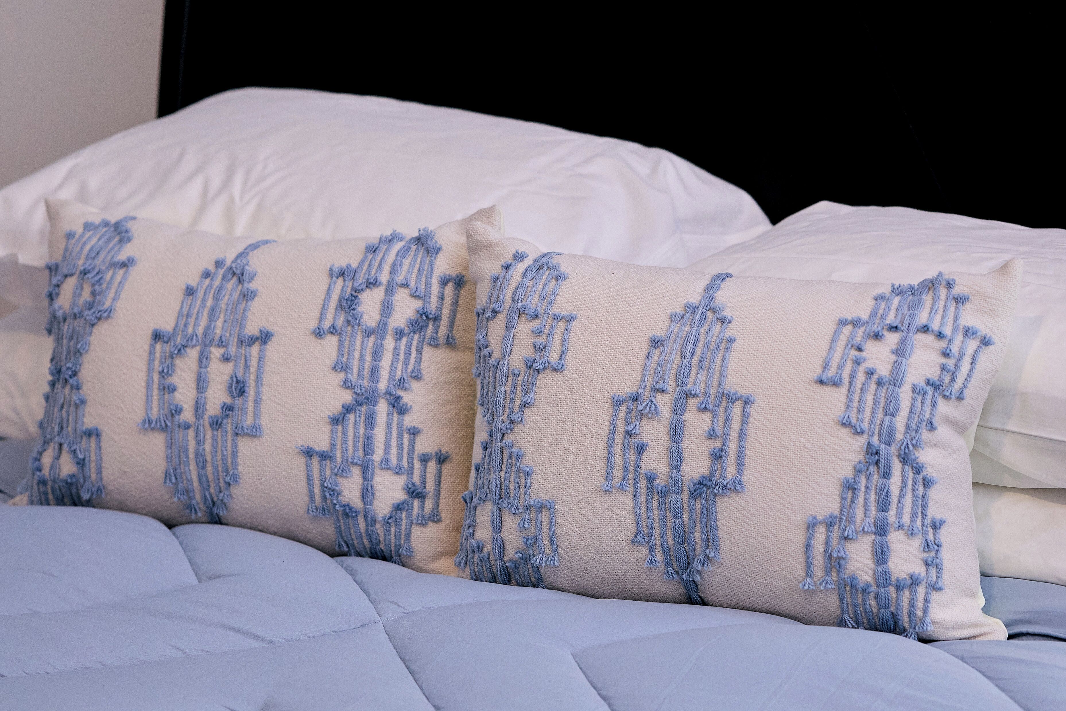 Una cama con almohadas blancas y una manta azul.