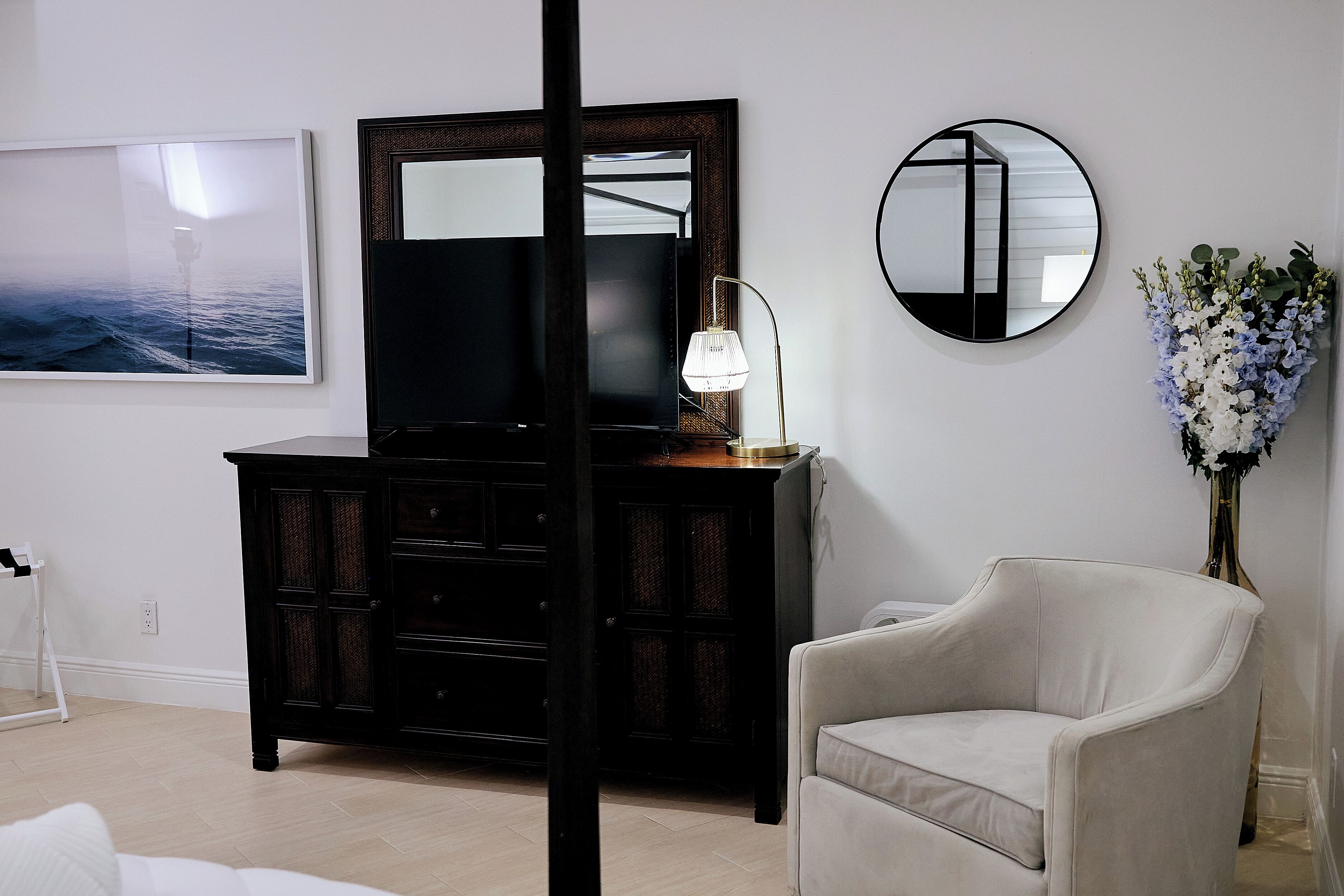A room with a large mirror, a dresser, a lamp, and a chair.