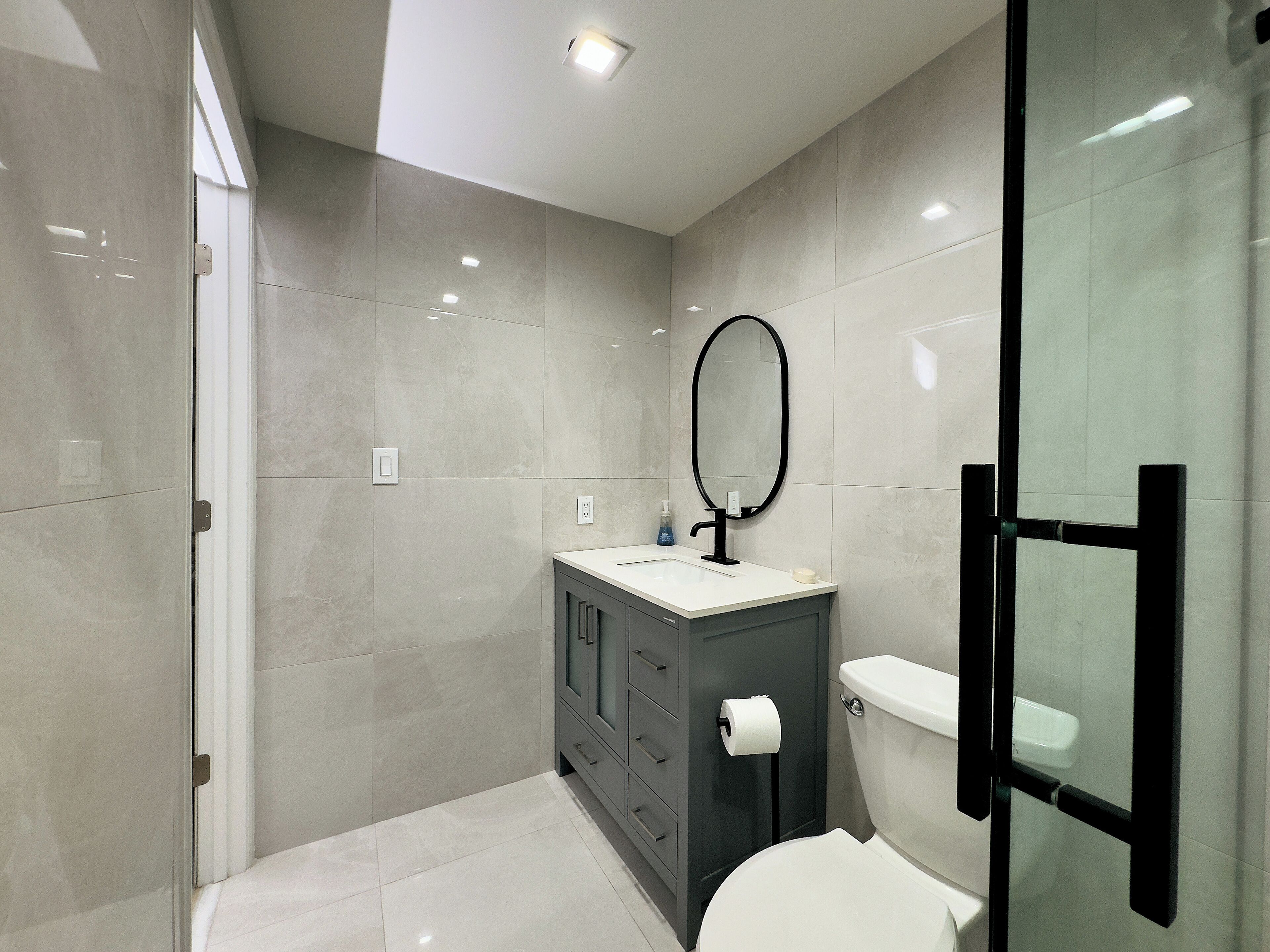 A modern bathroom with a glass shower enclosure, a toilet, a vanity with a mirror, and a toilet paper holder.