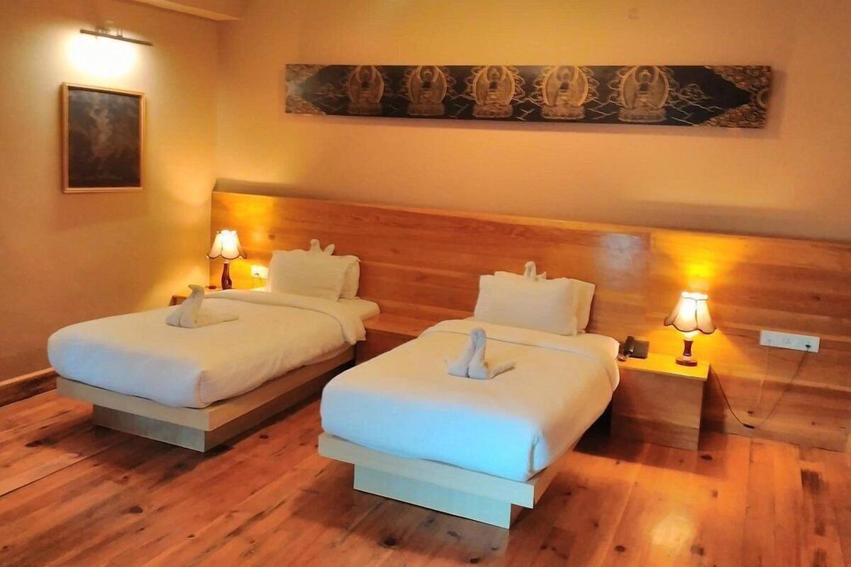 A hotel room with two beds, wooden flooring, and wall-mounted lamps.