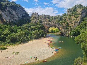 A river with boats, a beach, and a natural rock arch.