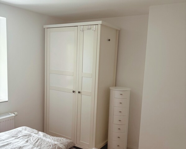 Un dormitorio con un armario blanco grande, una cómoda alta con cajones y una cama con una colcha estampada.