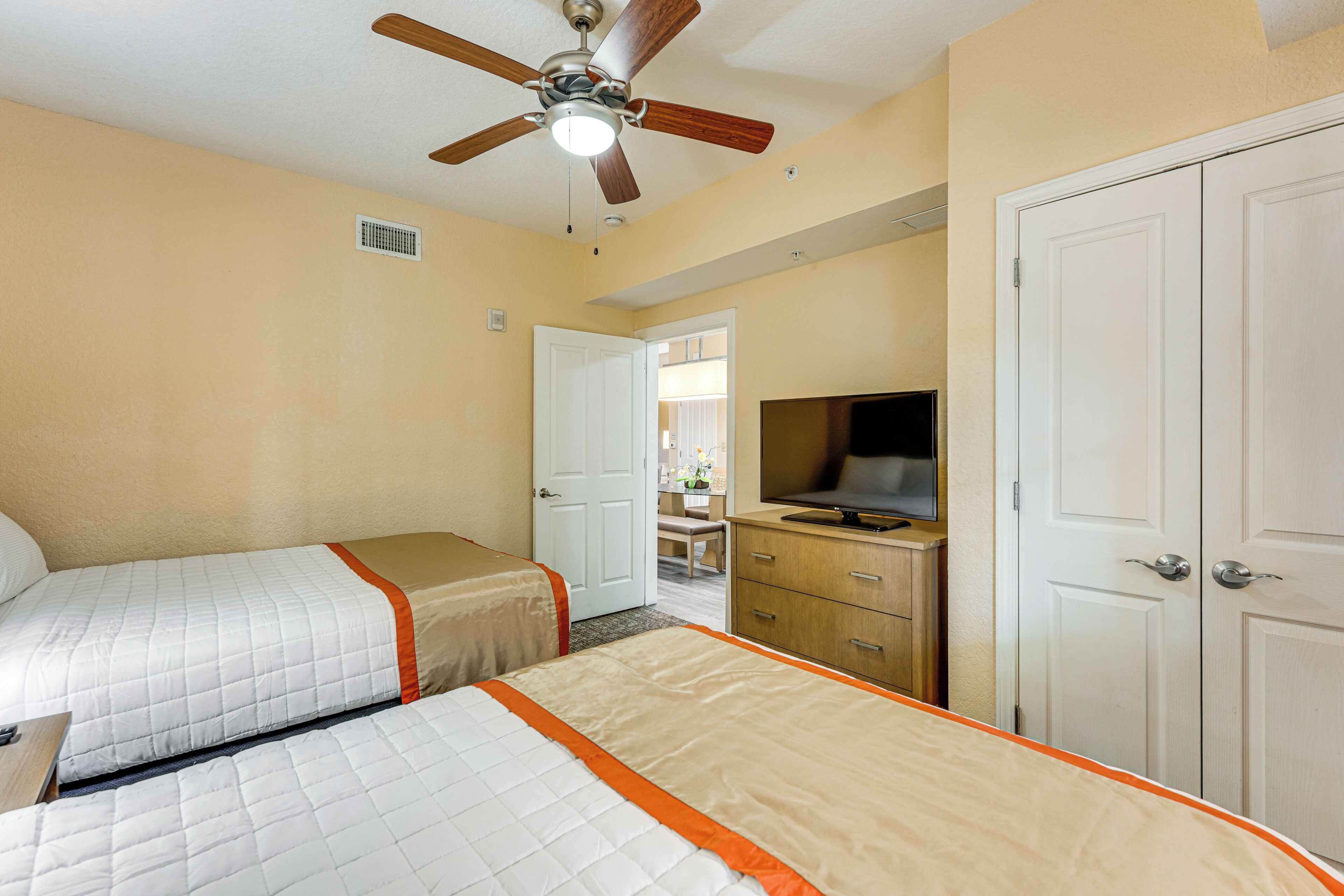A hotel room with two beds, a ceiling fan, a television, and a wardrobe.