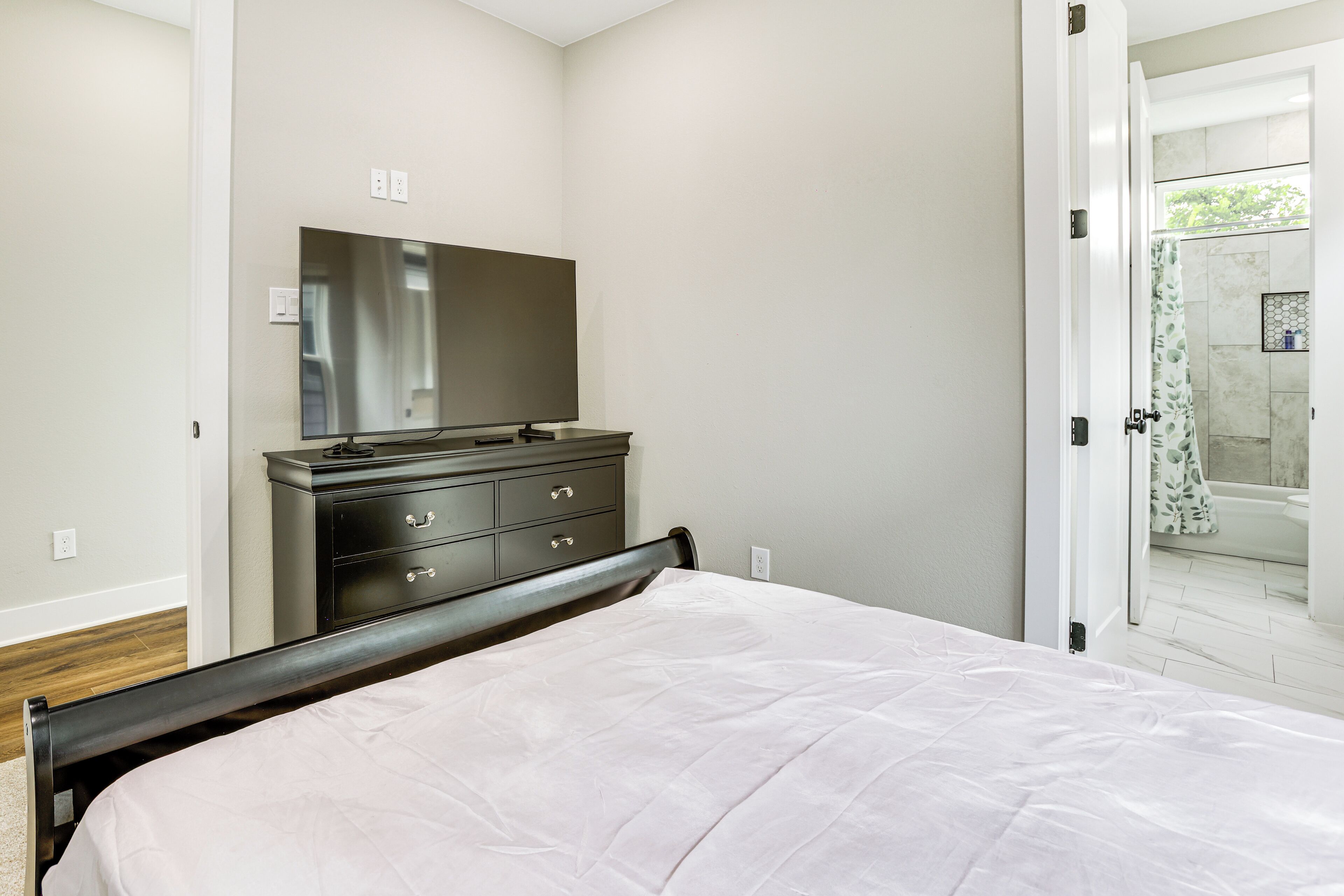 A bedroom with a bed, a dresser, and a mirror. There is a door leading to a bathroom with a shower and a bathtub.