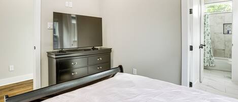 A bedroom with a bed, a dresser, and a mirror. There is a door leading to a bathroom with a shower and a bathtub.