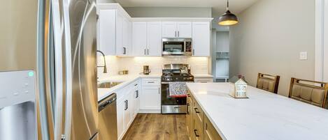 Una cocina moderna con electrodomésticos de acero inoxidable, muebles blancos y suelo de madera.