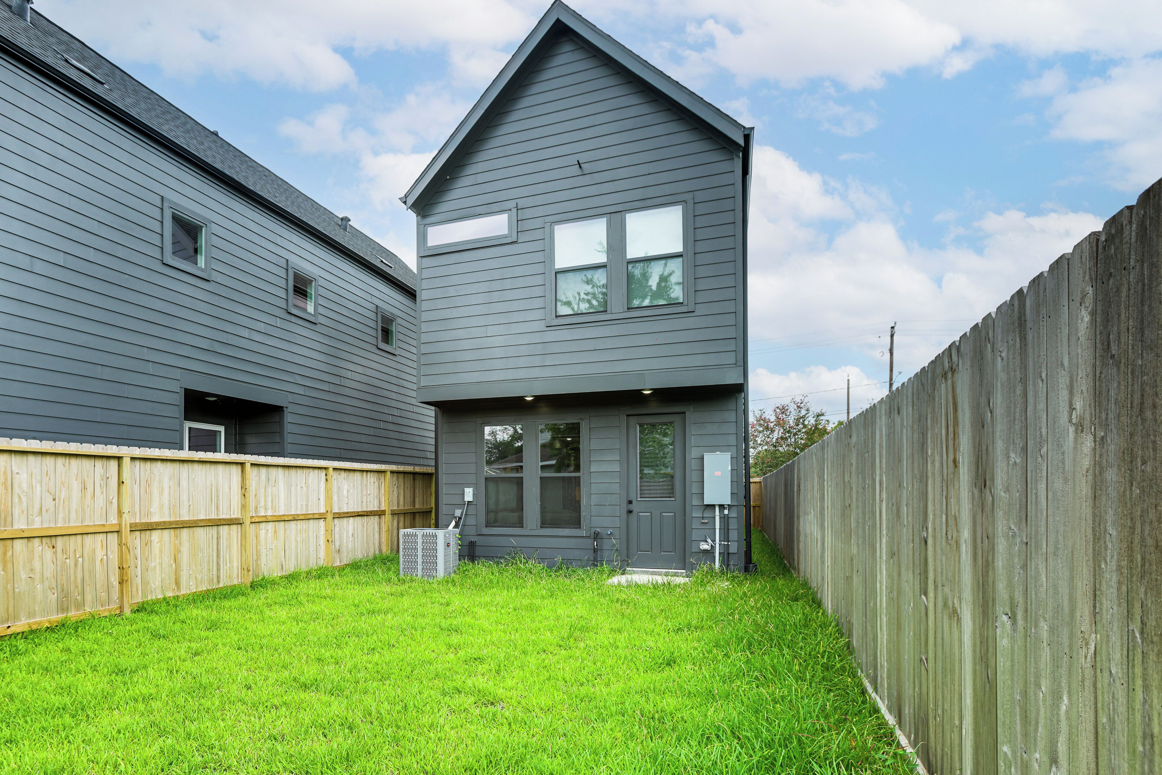A two-story house with a grey exterior, a fenced backyard, and a front door with a small porch.