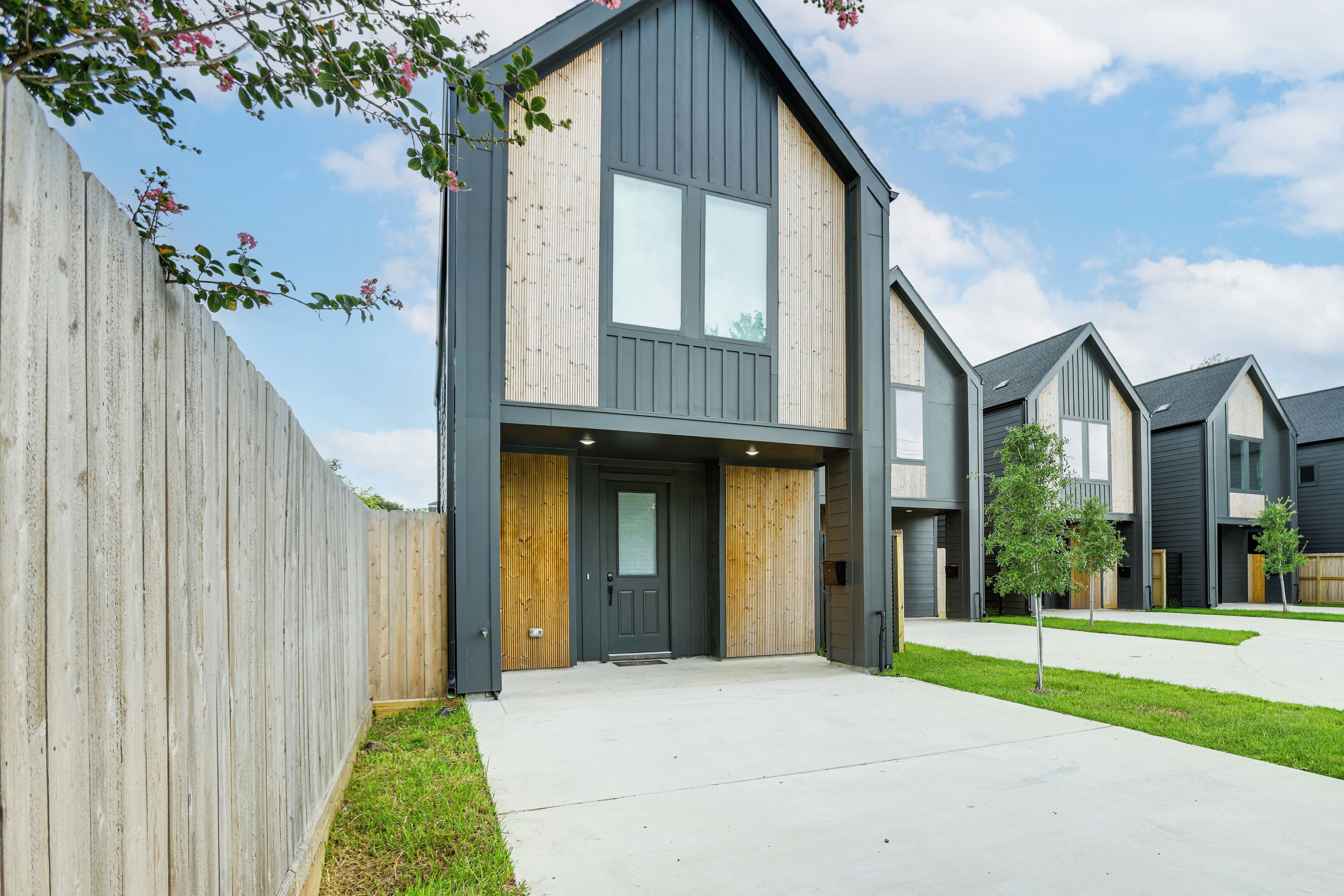 A modern two-story residential building with a front entrance, a wooden fence, and a well-maintained lawn.