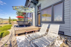 A deck with two lounge chairs and two umbrellas, a wooden table, and a view of the surrounding landscape. - Grand Elk Golf Club On-site: Mtn-view Home w/ Deck (Granby)