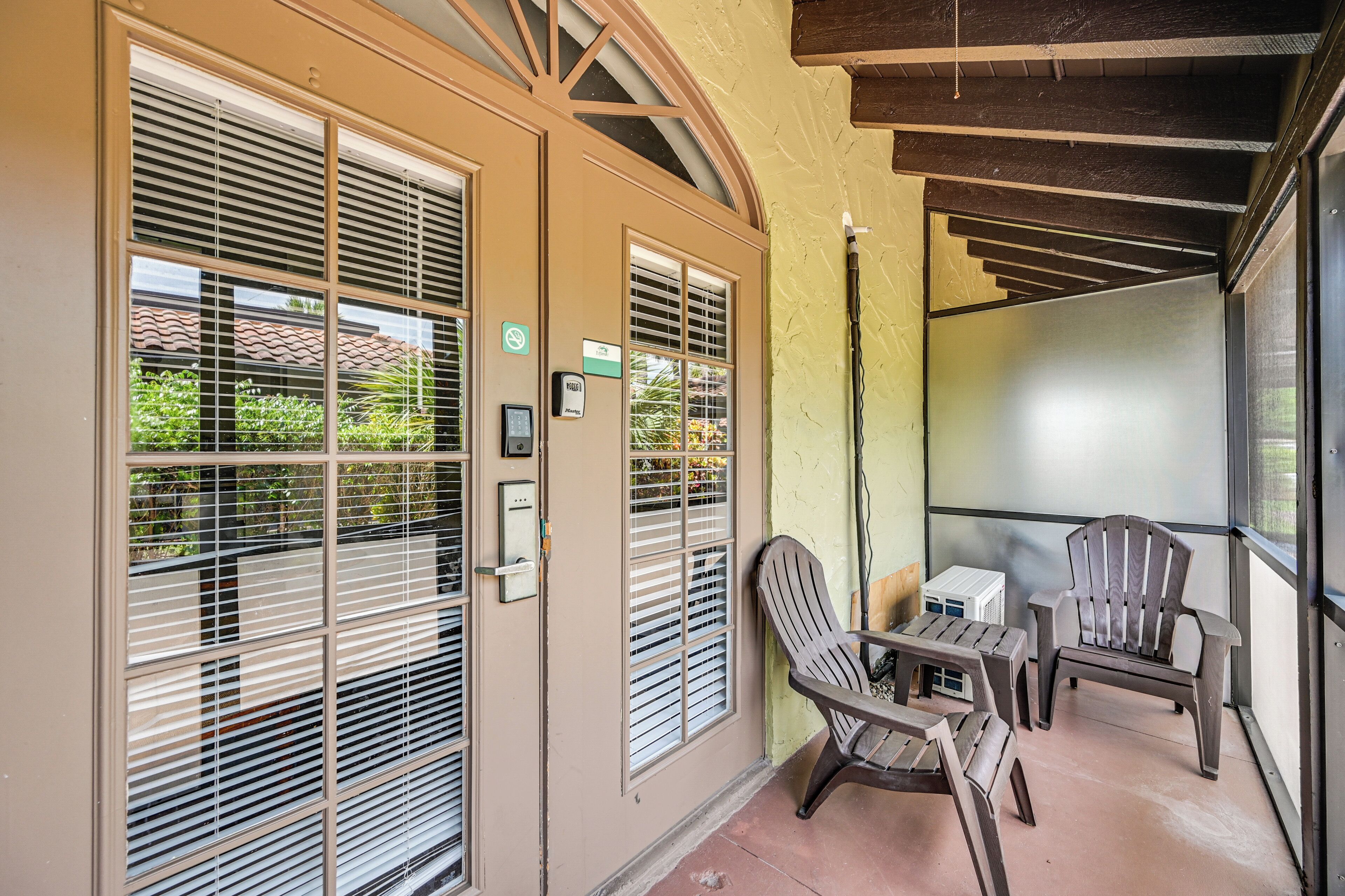 A balcony with two chairs and a table, a door with a window, and a wall-mounted air conditioning unit.