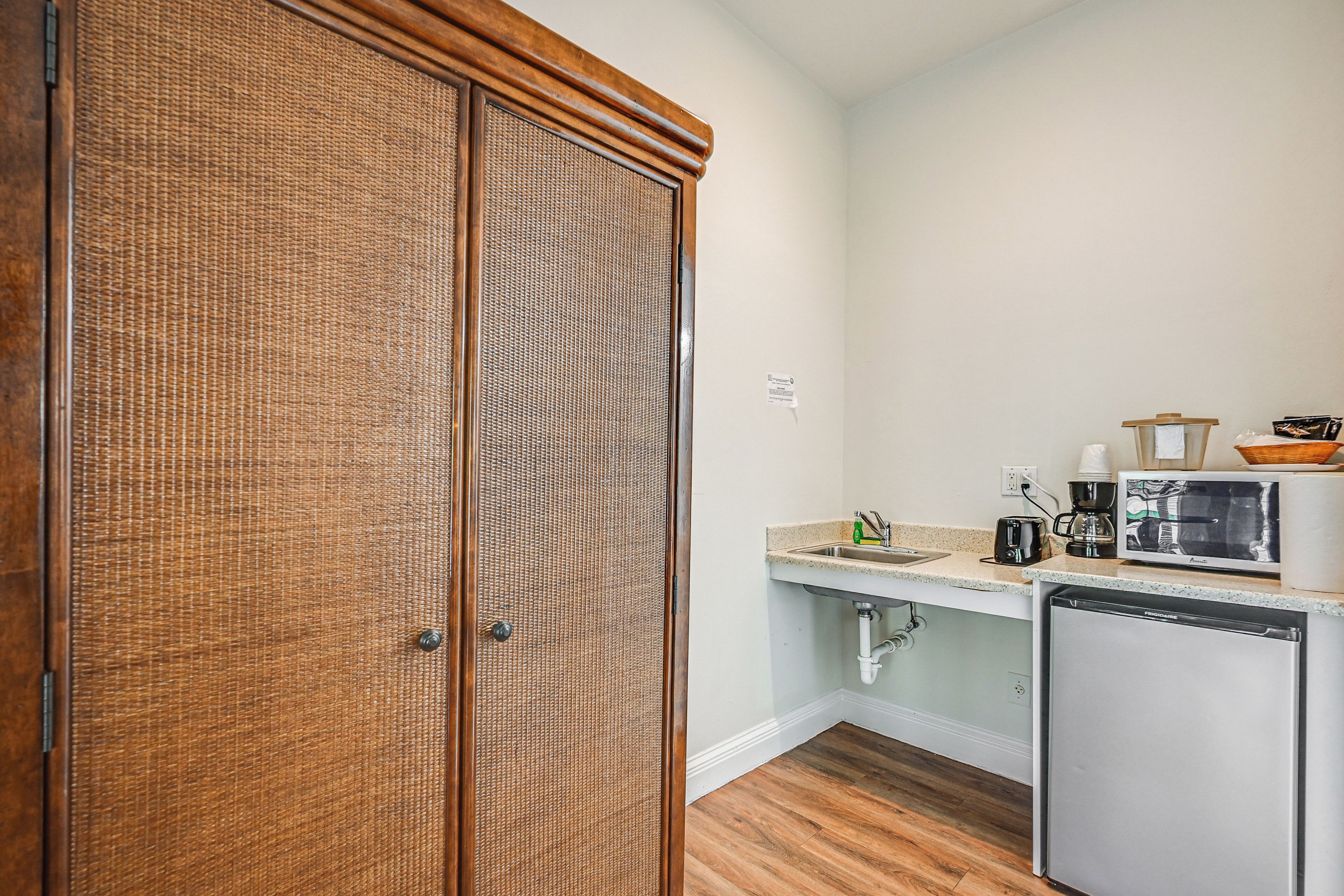 Una cocina compacta con puerta de madera, una encimera con fregadero, cafetera, microondas y refrigerador pequeño.