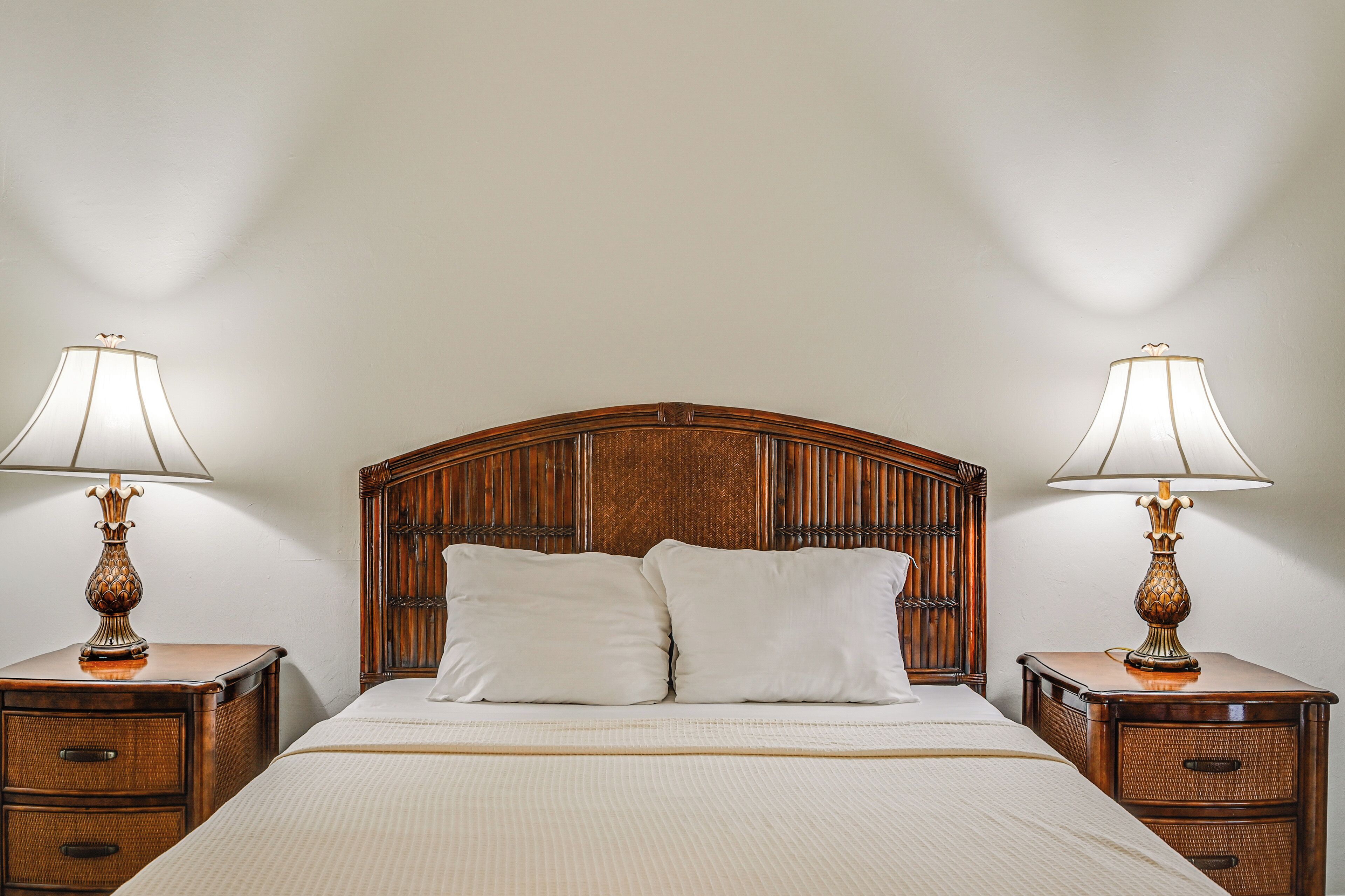 Una cama bien hecha con dos almohadas, flanqueada por dos mesitas de noche con lámparas, en una habitación con cabecero de madera.