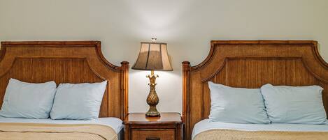 A double room with two wooden headboards, a nightstand with a lamp, and a bed with a beige blanket.