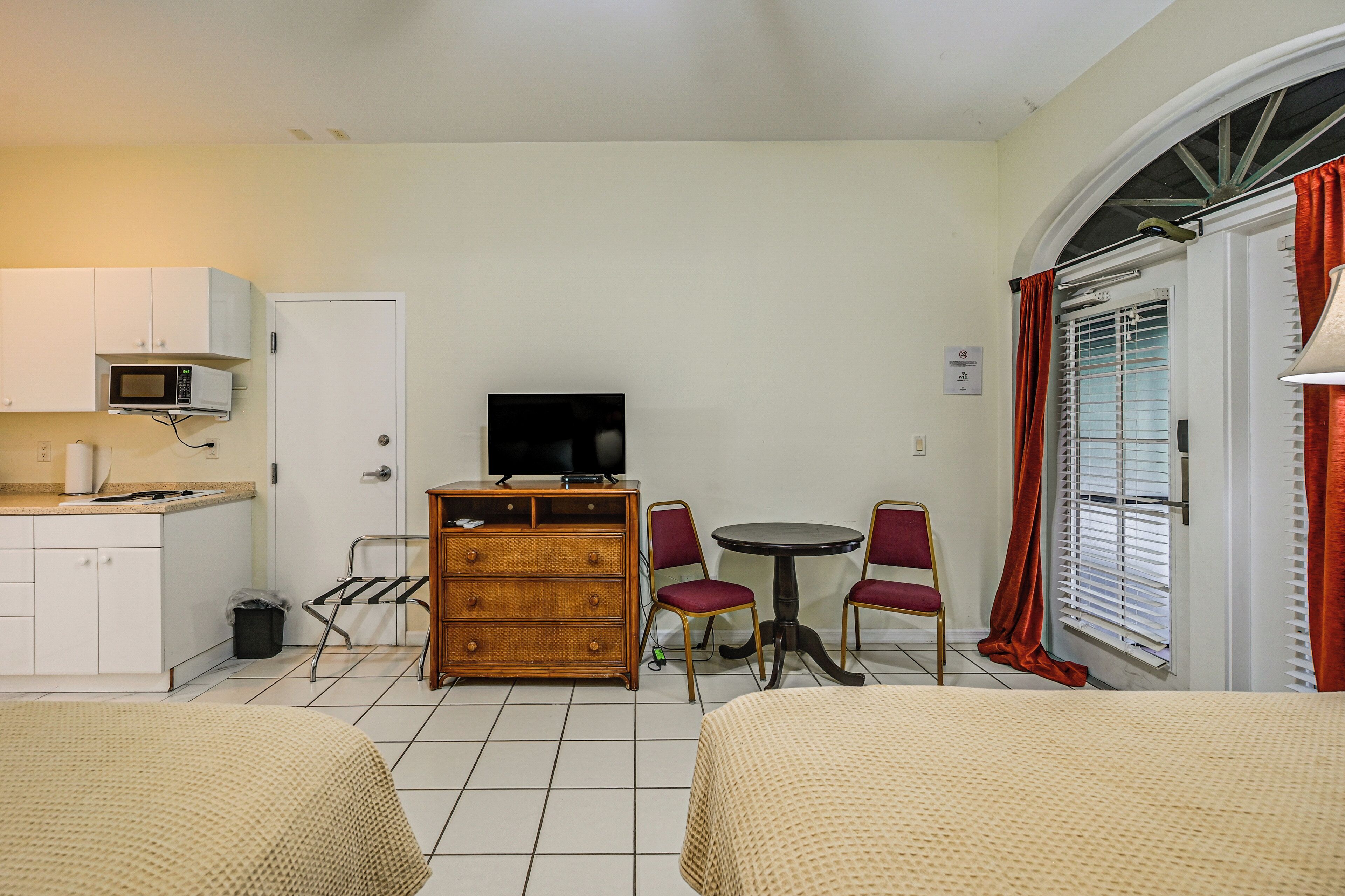 A hotel room with two beds, a television, a small dining table with chairs, a microwave, and a cabinet.