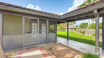 A covered patio area with a tiled roof, a concrete floor, and a small garden with a palm tree.