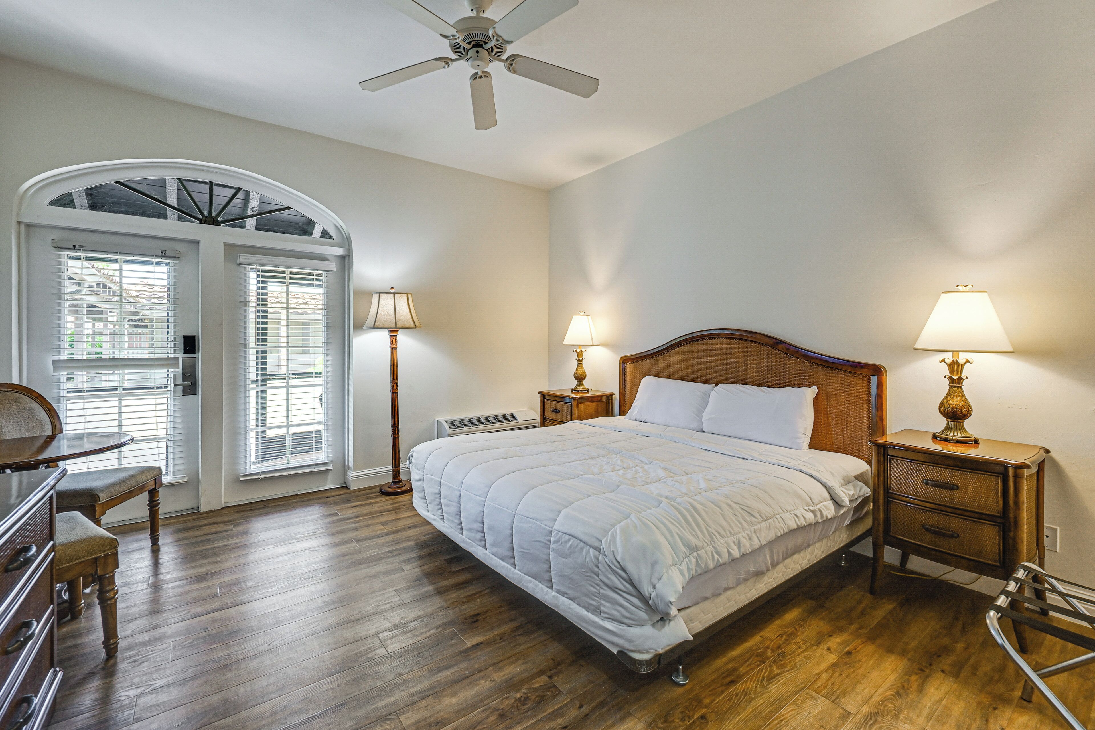 Quarto com uma cama grande, duas luminárias de cabeceira, um ventilador de teto e uma cômoda de madeira.