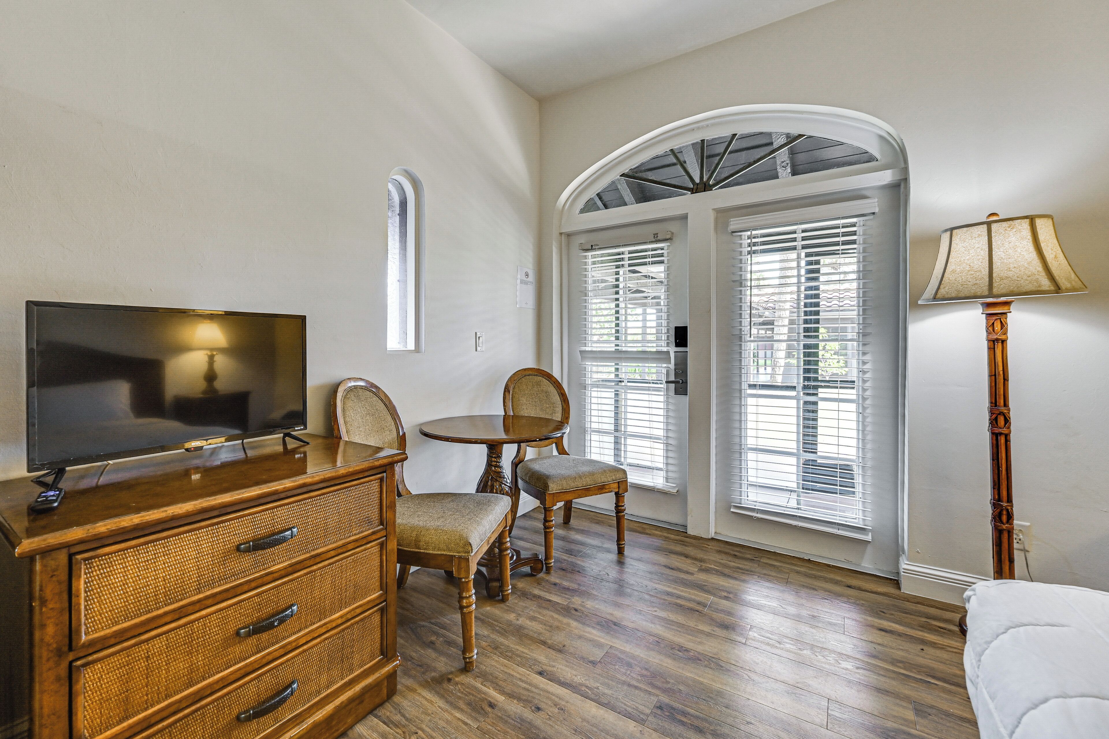 A room with a wooden dresser, a television, a dining table with chairs, and a lamp.