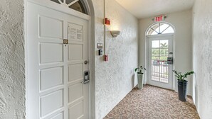A hallway with a white door, an exit sign, a security camera, and a potted plant. - Marina, Heated Pool & Game Room: Naples Condo! (Naples)