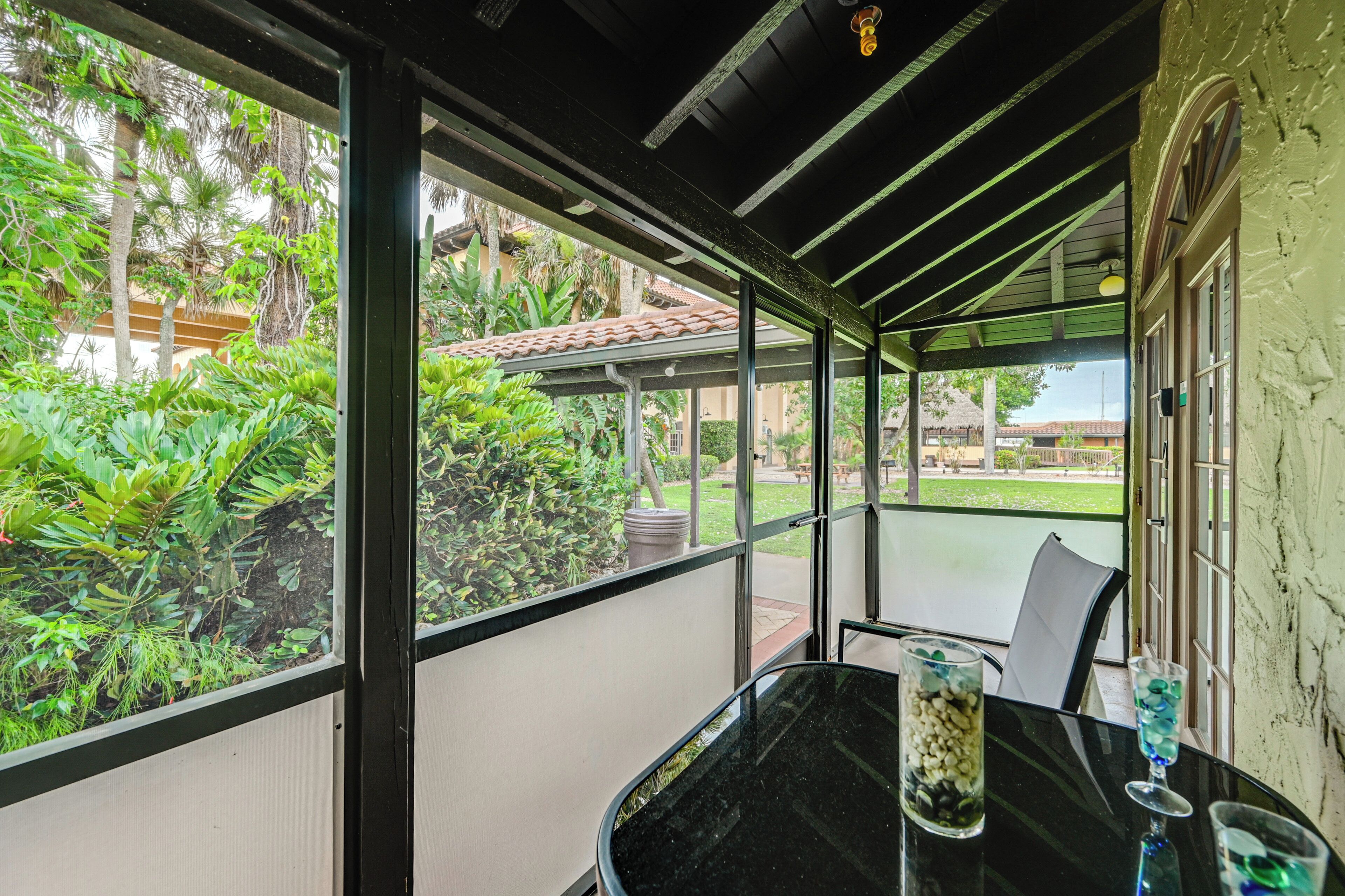 Un espace extérieur aménagé, abrité et doté de tables et de chaises, entouré de murs de verre et offrant une vue sur une végétation luxuriante.