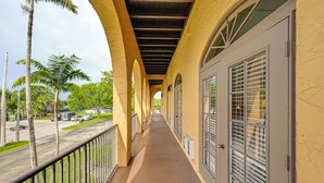 A covered outdoor corridor with a concrete floor, metal railings, and a view of a street with palm trees and parked vehicles. - Direct 10,000 Islands Access: POI Resort Studio (Naples)