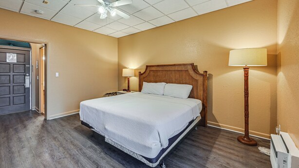 A hotel room with a large bed, wooden headboard, two bedside lamps, a ceiling fan, and a door to the left. - Naples Studio w/ 10K Islands Access + Marina View (Naples)