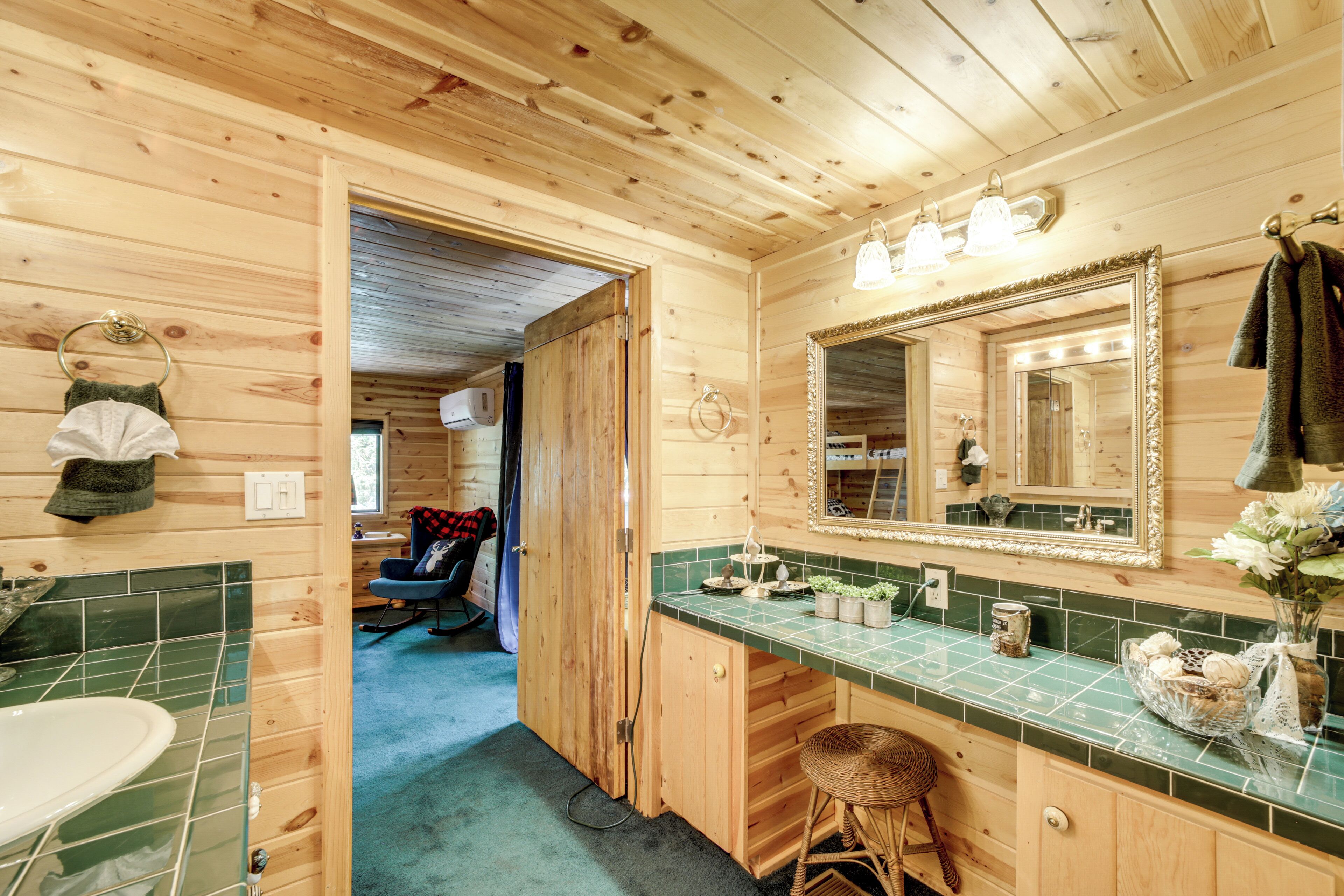 Baño de cabaña de madera con lavamanos, espejo y encimera con azulejos verdes.