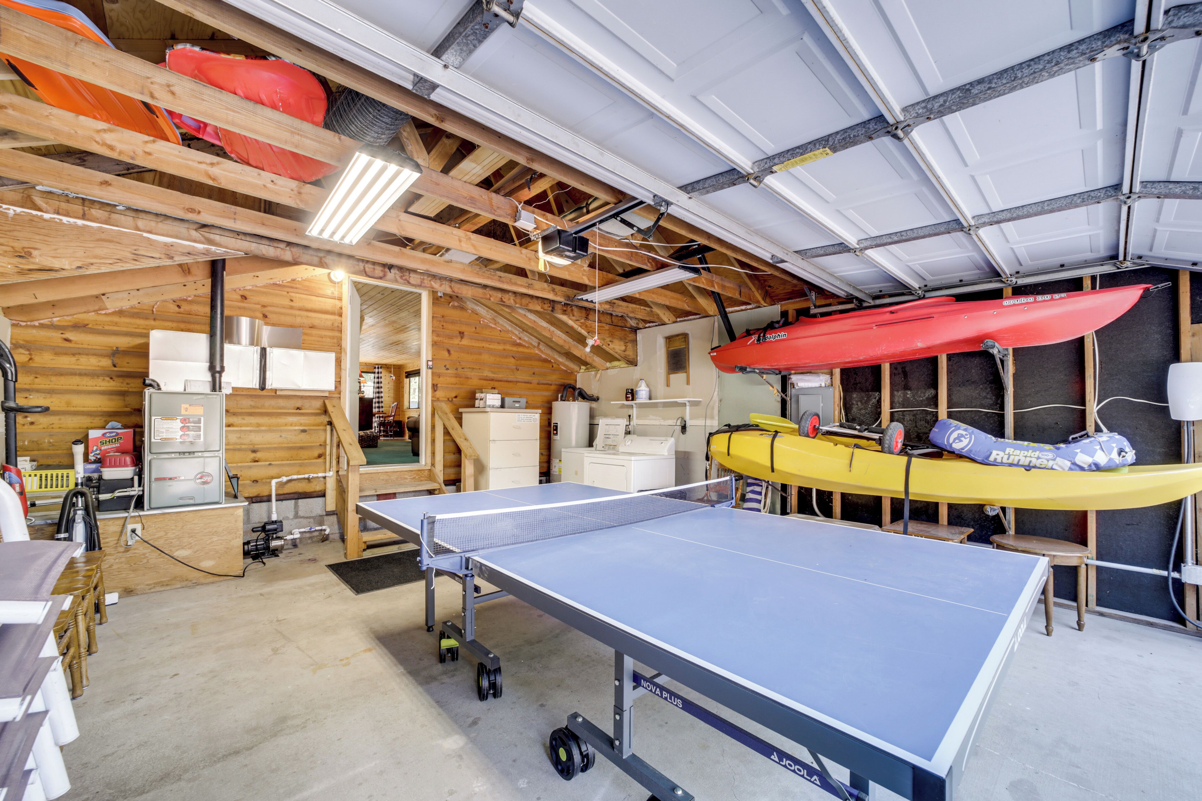A spacious room with a ping pong table, wooden ceiling beams, and kayaks stored against the wall.